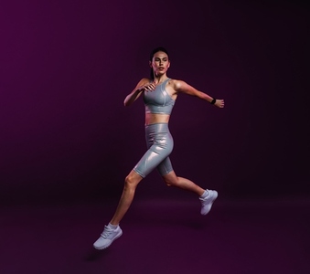 Young slim female in silver fitness attire running against a magenta background