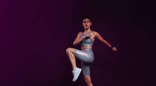 Slim woman in silver fitness clothes warming up her legs in studio against magenta backdrop
