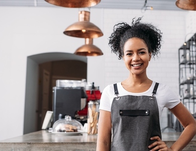 Smiling and confident barista looking at camera while standing in coffee shop