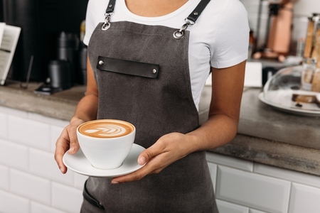 Cropped shot of an unrecognizable barista holding a cup of coffee  Waitress in an apron with a freshly prepared cappuccino