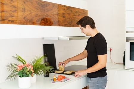 Adult man standing near cooking range and toasting bread slices in kitchen
