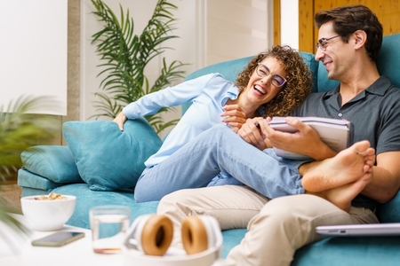 Happy couple with notebook sitting on sofa at home while laughing joyfully