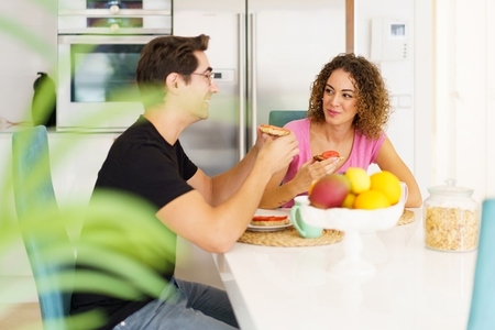 Happy adult couple sitting at dining table and talking during breakfast at home