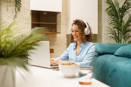 Smiling woman using laptop while doing remote work in living room