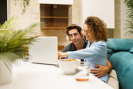Happy couple cuddling while using laptop and spending time at home