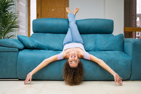 Happy woman woman lying upside down on couch at home