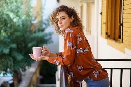 Young woman with coffee cup leaning on balcony of house