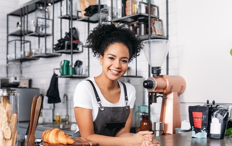 Beautiful female barista looking at camera  Cheerful waitress in an apron standing at a counter in a cafe
