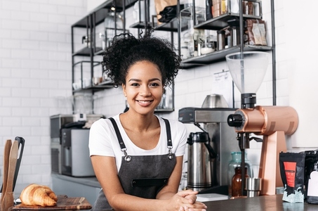 Confident barista with curly hair looking at camera standing at a counter