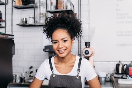 Close up of a young smiling barista with curly hair wearing an apron