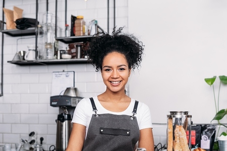 Portrait of a young smiling female barista with curly hair looking at camera