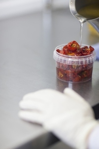 Close up of a worker hand pouring oil in a plastic container filled with sun dried tomatoes