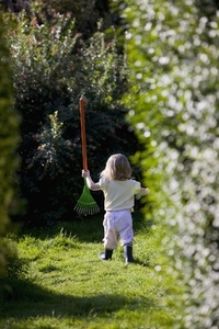 Back view of a young girl walking in a garden holding a toy rake