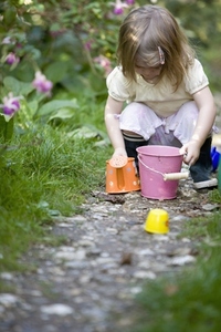 Young girl crouching in a garden playing with gardening toys