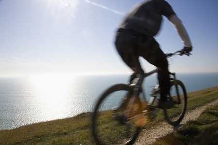 Back view of a man cycling on a costal path by the ocean