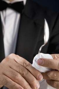 Close up of a waiter polishing a silver spoon with a white napkin