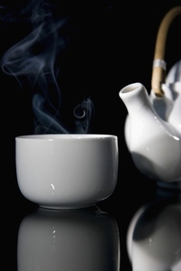 Close up of a steaming green tea teacup and detail of a teapot with wooden handle
