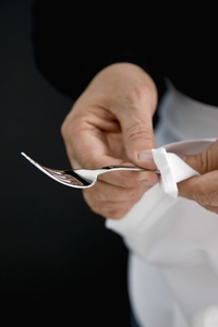 Close up of a waiter hands polishing a silver fork with a white napkin