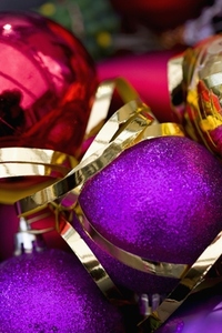 Extreme close up of red and purple Christmas baubles and a gold ribbon