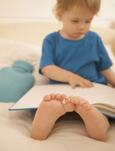Young boy sitting in bed with an open book over is legs and feet