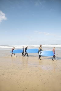 Men and children walking on a beach carrying surfboards
