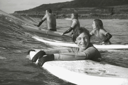 Smiling teenaged boy in the sea holding on to his surfboard