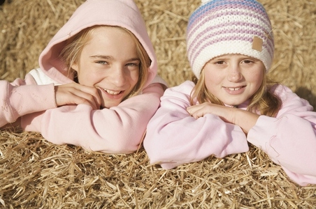 Two young girls leaning on bale of hay smiling