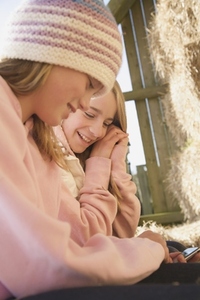 Two young girls sitting in front of hay bales using a cell phone