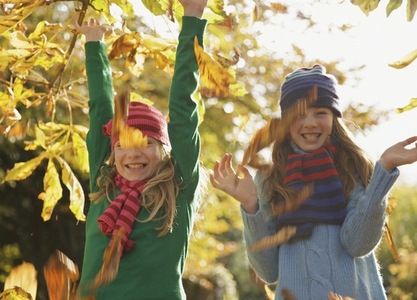 Two smiling girls throwing leaves in the air