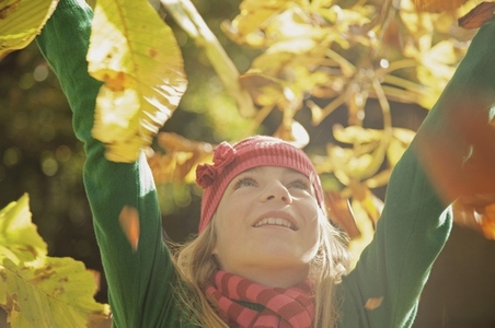 Close up of a smiling young girl with her arms in the air surrounded by leaves