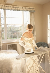 Bride in white wedding gown ironing her veil