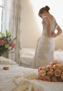 Close up of a bouquet of roses and bridal gloves lying on a bed with bride undressing
