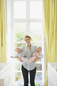 Smiling Mother Holding Twin Babies in Nursery