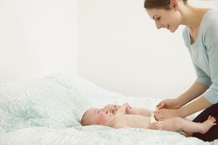 Smiling Mother Kneeling on Bed Playing Twin Babies