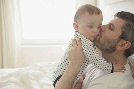 Father Kissing Baby Boy in Bedroom