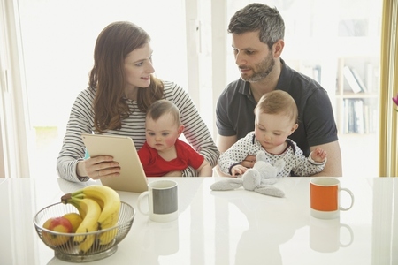 Couple Sitting at Table with Baby Twins Using Digital Tablet