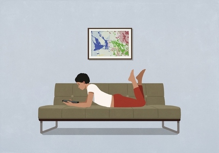 Woman relaxing using digital tablet on living room sofa at home