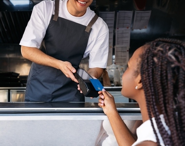 Cropped shot of a food truck owner holding a POS terminal while a female customer pays by a contactless card