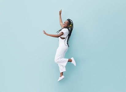 Happy woman in white casual clothes jumping against a blue wall  Young female with braids jumps outdoors