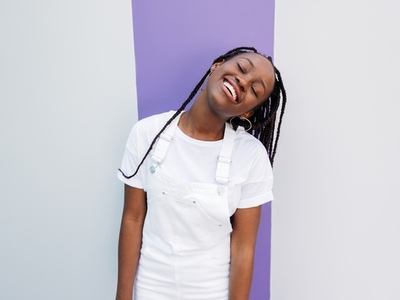 Young cheerful female in white casual clothes standing outdoors a white wall with a magenta stripe