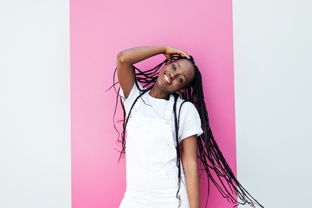 Portrait of a positive girl in white overall standing at wall with pink stripe and looking at camera
