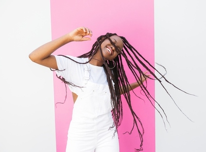 Girl with long braids having fun and dancing at a wall with pink stripe