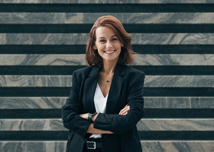 Happy female with ginger hair in formal wear looking at camera  Young confident middle aged woman with crossed arms standing outdoors and smiling