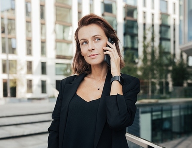 Portrait of a middle aged female looking away while taking on a mobile phone  Corporate person with ginger hair standing outdoors and having a conversation by smartphone