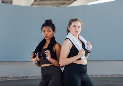 Two plus size women in fitness wear standing back to back looking at camera  Two young females with towels posing after a workout