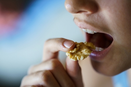 Unrecognizable girl with mouth open about to eat healthy walnut
