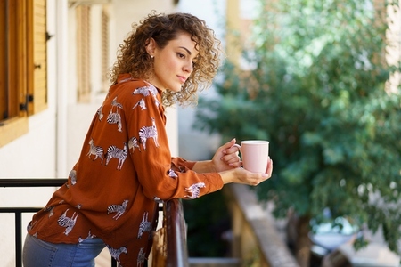 Young woman with coffee cup standing on balcony of house