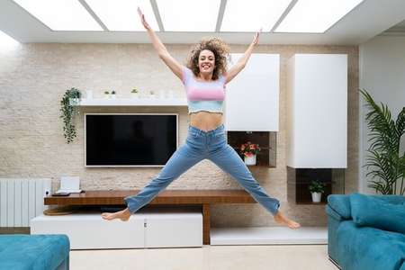 Excited woman jumping and raising hands up at home