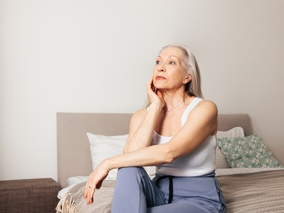 Frustrated senior female sitting on a bed in living room