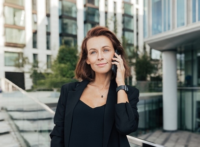 Portrait of a cheerful middle aged businesswoman talking on a smartphone wearing black clothes